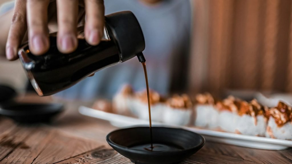 A person pouring soy sauce into a dish